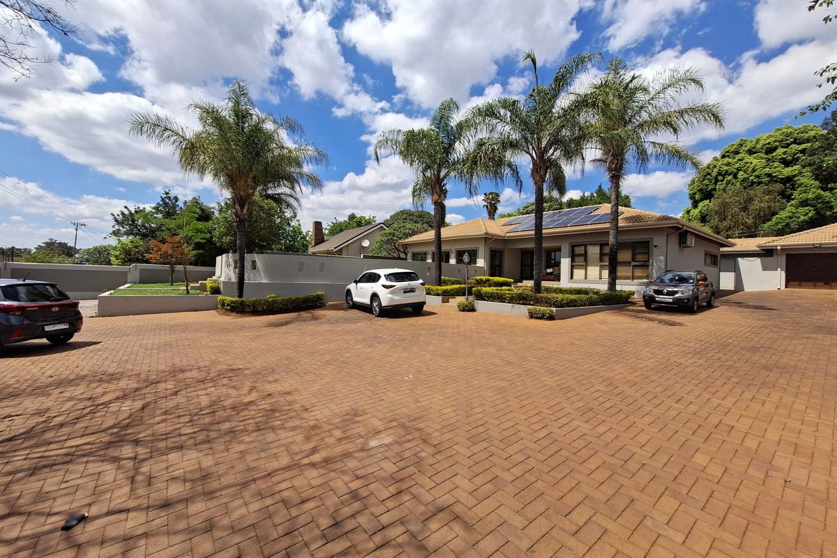 Spacious front exterior featuring a large paved driveway, well-maintained garden beds, and a house roof equipped with solar panels.