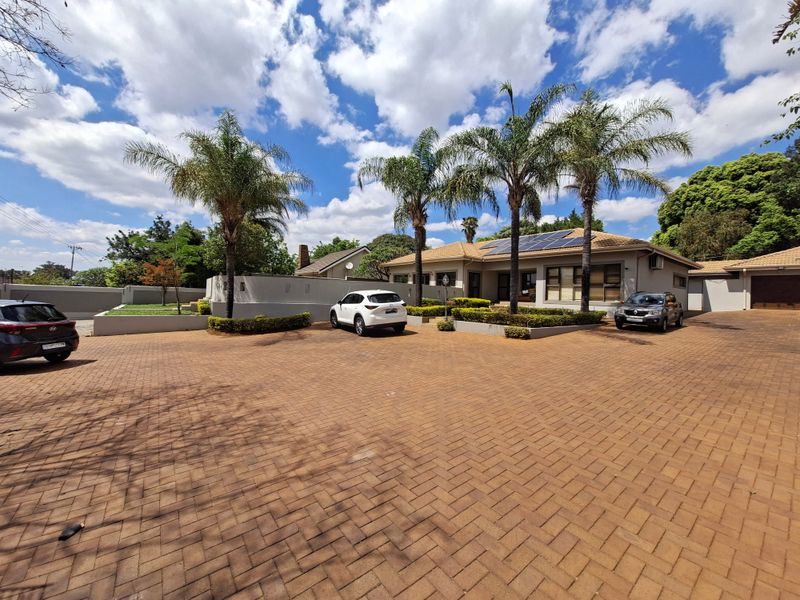 Spacious front exterior featuring a large paved driveway, well-maintained garden beds, and a house roof equipped with solar panels.