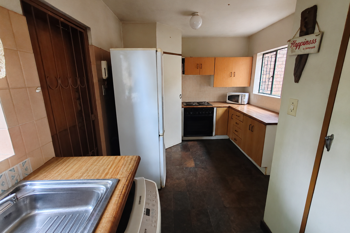 A functional kitchen featuring wooden cabinetry, laminate countertops, a built-in oven and hob, and a stainless steel sink.