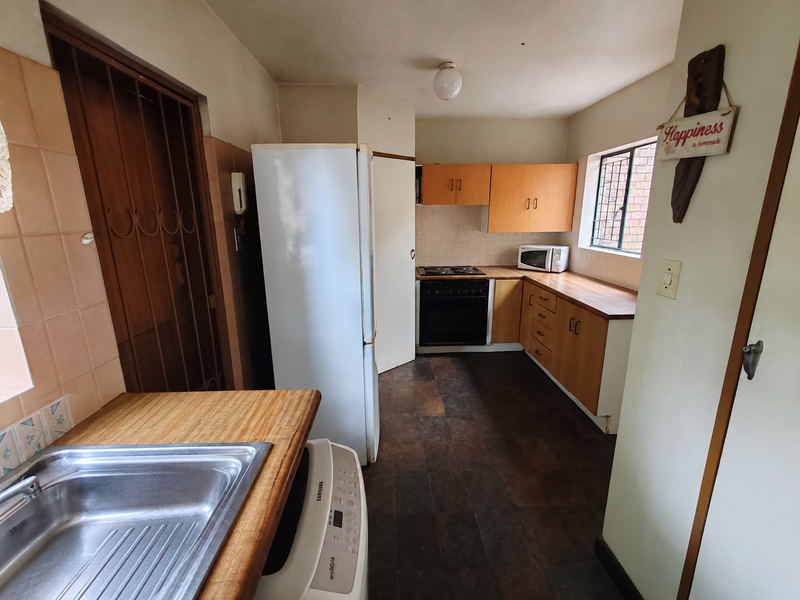 A functional kitchen featuring wooden cabinetry, laminate countertops, a built-in oven and hob, and a stainless steel sink.
