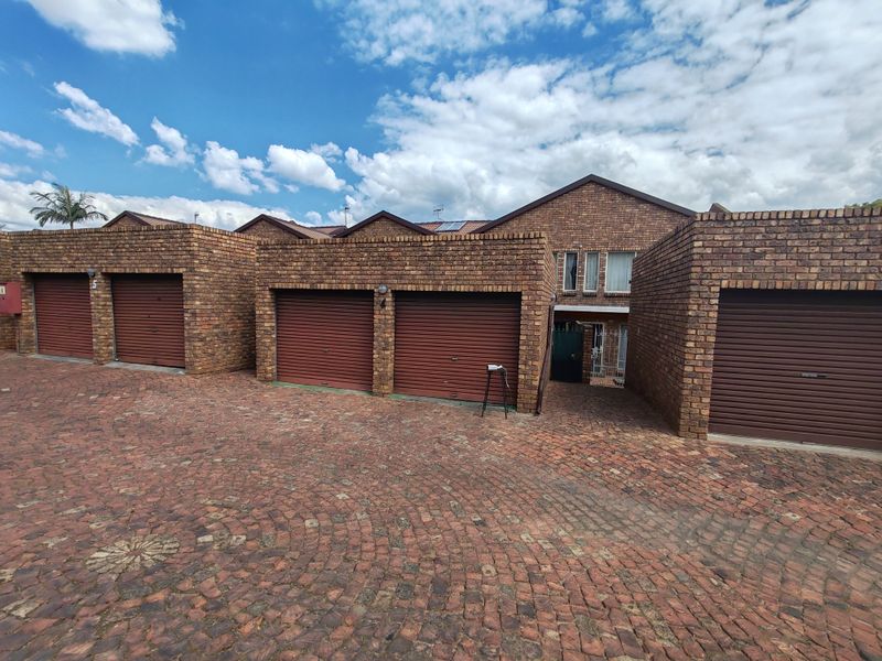 Front exterior view of a townhouse complex featuring face brick construction, multiple roller shutter garage doors, and a paved driveway.