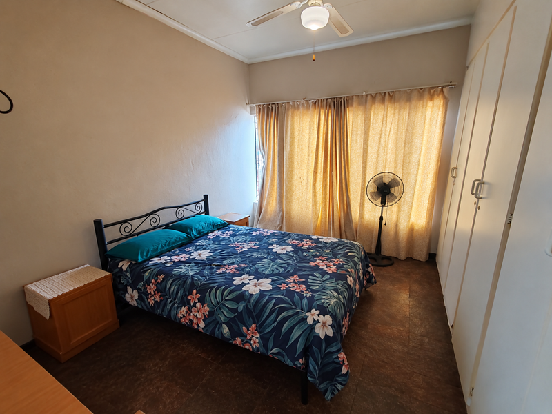 A functional bedroom featuring built-in cupboards, tiled flooring, and a ceiling fan, offering a comfortable and practical living space.