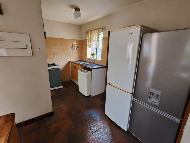 A functional kitchen featuring tiled splashbacks, built-in cabinetry, and a stainless steel sink, with potential for modernization to enhance the space.