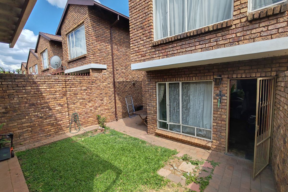 A private rear courtyard featuring a face brick facade, paved patio area, and a small lawn section with a secure entrance gate.