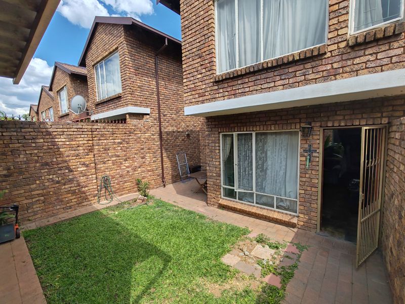 A private rear courtyard featuring a face brick facade, paved patio area, and a small lawn section with a secure entrance gate.