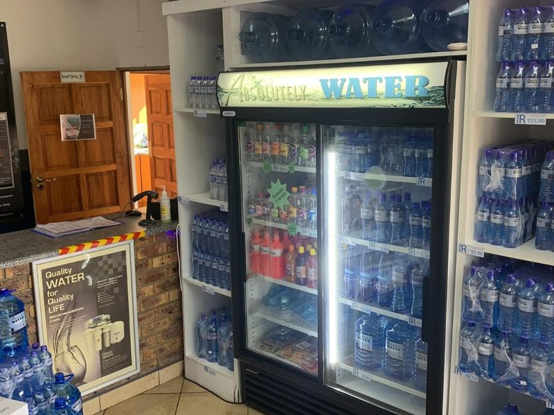 A commercial retail space featuring built-in shelving units, a service counter with brick detailing, and tiled flooring, currently set up for water sales.