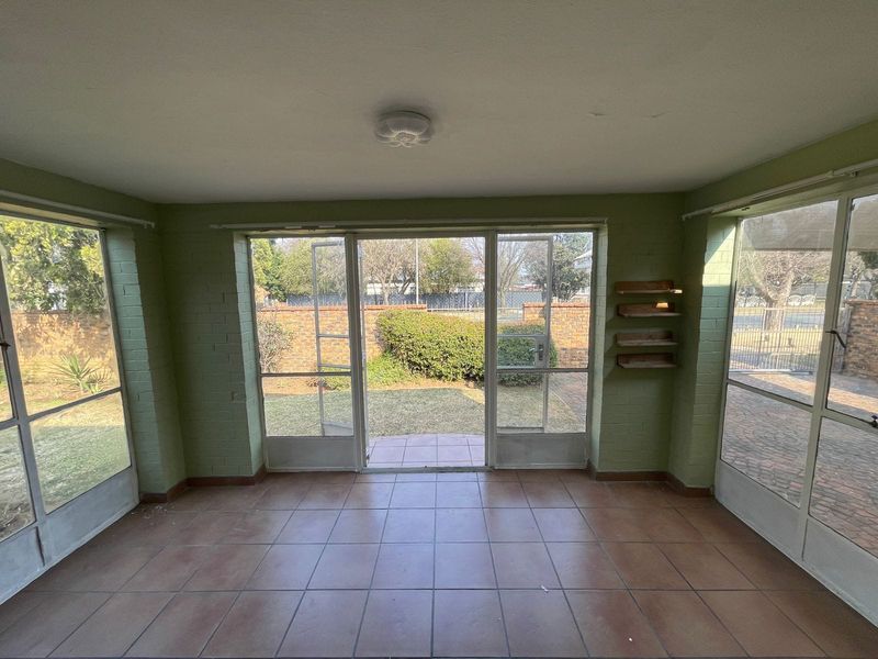 A sun-filled enclosed patio featuring tiled flooring, large glass windows, and direct access to the garden area.