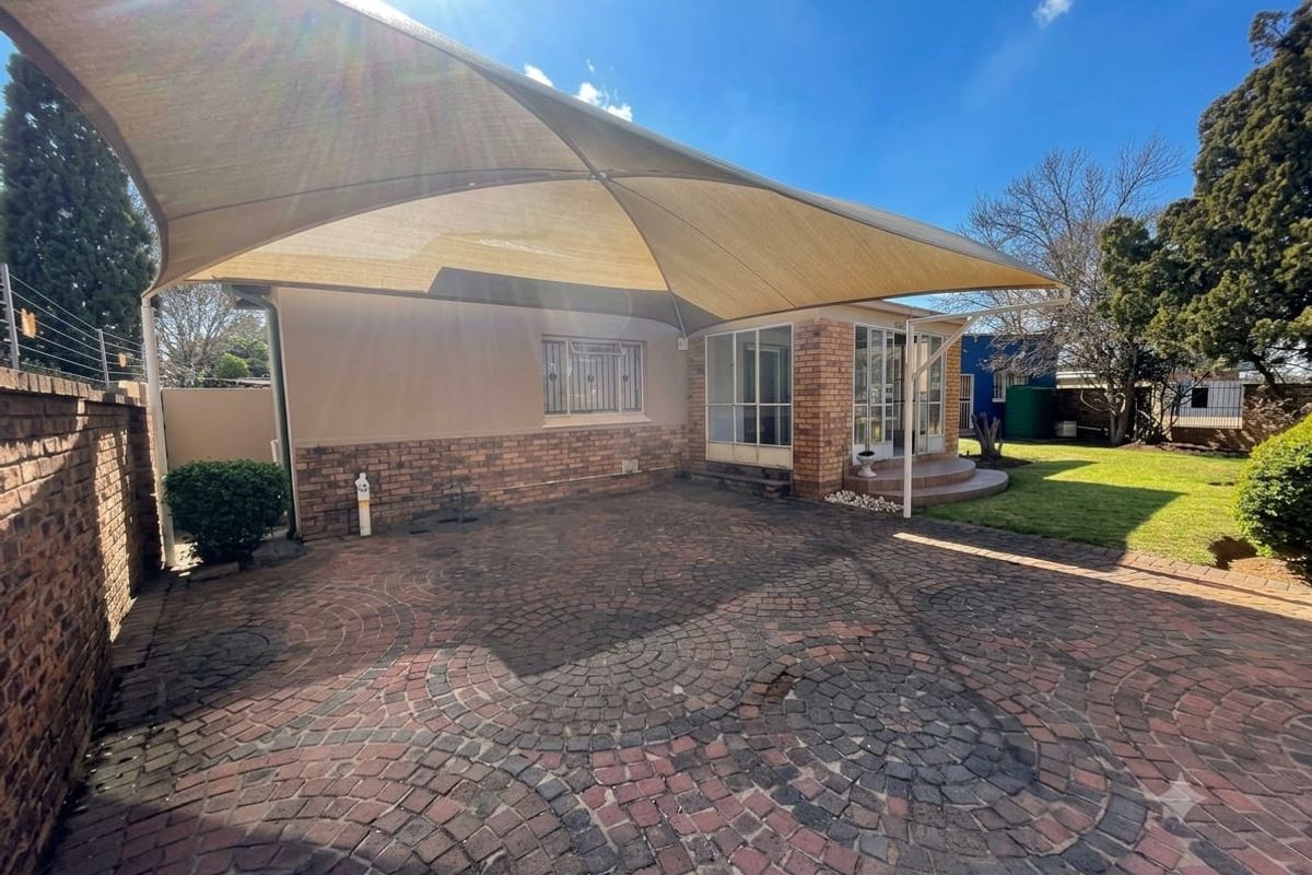 Rear exterior view featuring a paved driveway, a large shade sail covering the patio area, and a well-maintained garden lawn.
