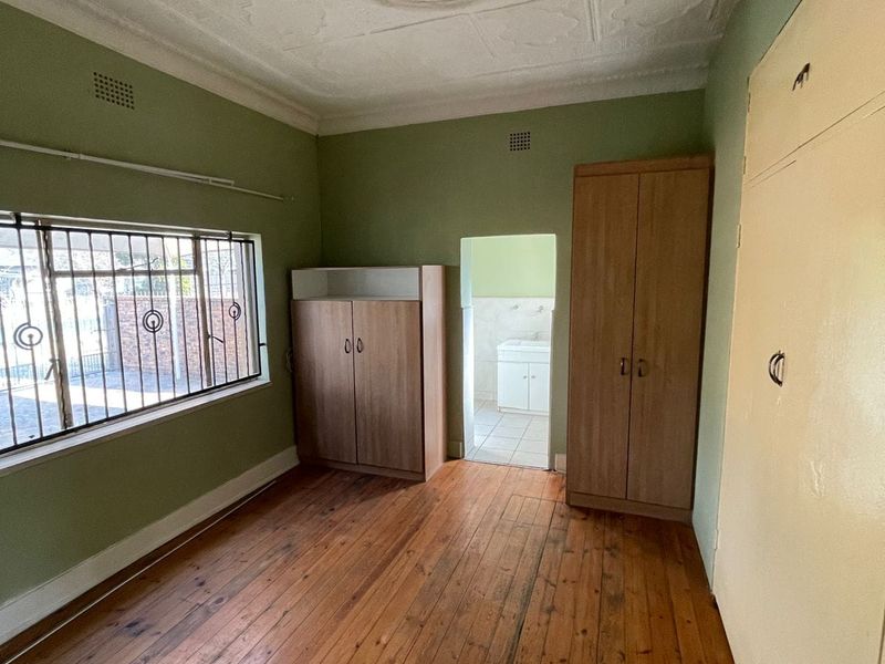A bedroom featuring original pressed metal ceilings, polished timber flooring, and built-in storage, with an adjoining small bathroom area.