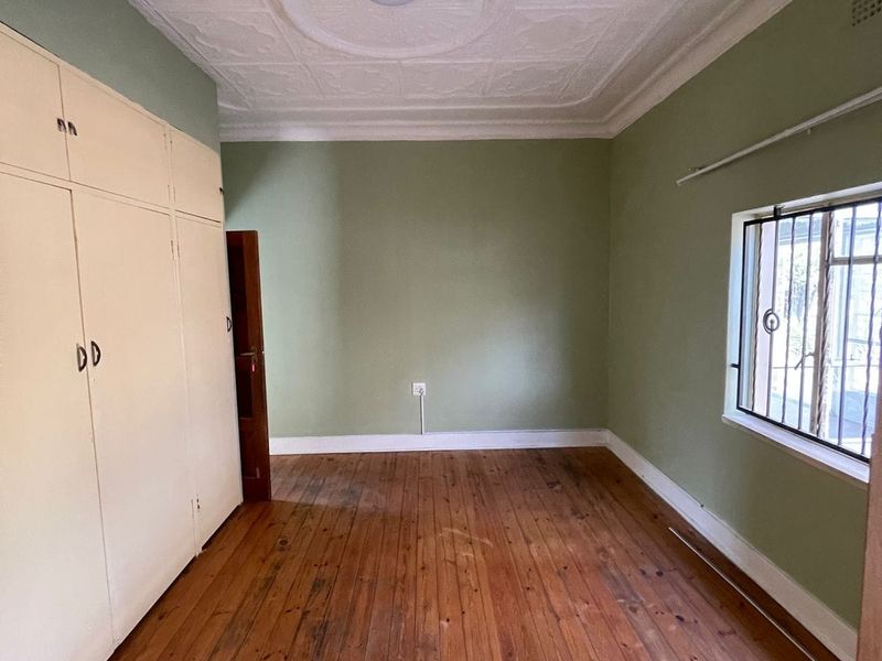 A vacant bedroom featuring original hardwood flooring, ornate ceiling detailing, and built-in storage cupboards, offering a classic foundation for renovation.
