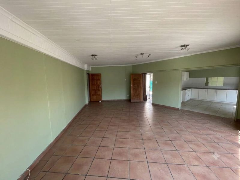 Spacious open-plan living area featuring tiled flooring and a timber panelled ceiling, seamlessly connecting to a functional kitchen space.