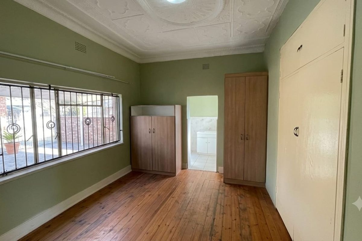 A spacious bedroom featuring original pressed metal ceilings, polished timber flooring, and built-in storage, with security bars installed on the windows.