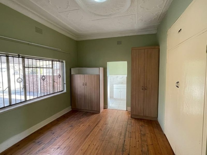 A spacious bedroom featuring original pressed metal ceilings, polished timber flooring, and built-in storage, with security bars installed on the windows.