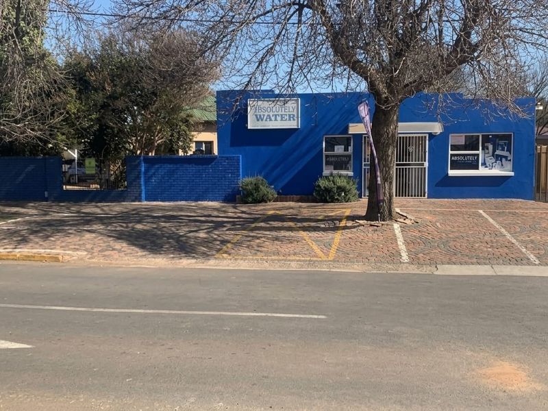 Front exterior view of a commercial property featuring a blue facade, paved parking area, and secure entrance gate.
