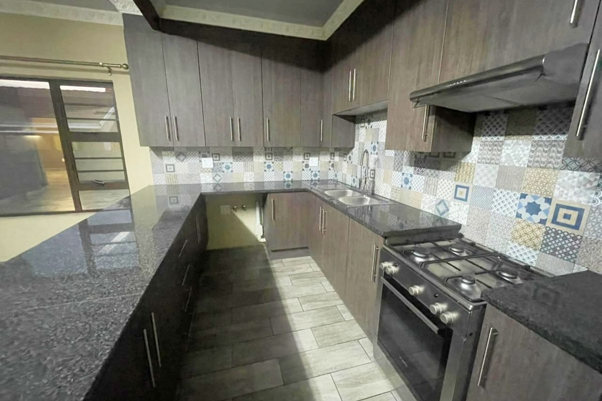 A modern kitchen featuring dark wood cabinetry, granite countertops, a gas stove with extractor, and a decorative tiled backsplash.