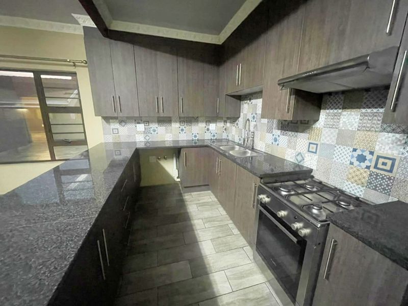A modern kitchen featuring dark wood cabinetry, granite countertops, a gas stove with extractor, and a decorative tiled backsplash.