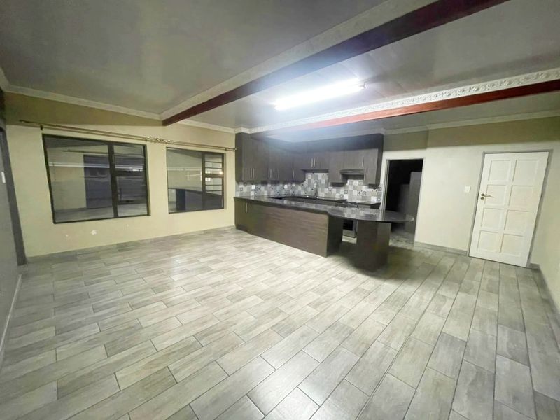 Spacious open-plan kitchen and living area featuring modern tiled flooring, dark wood cabinetry, granite countertops, and exposed ceiling beams.
