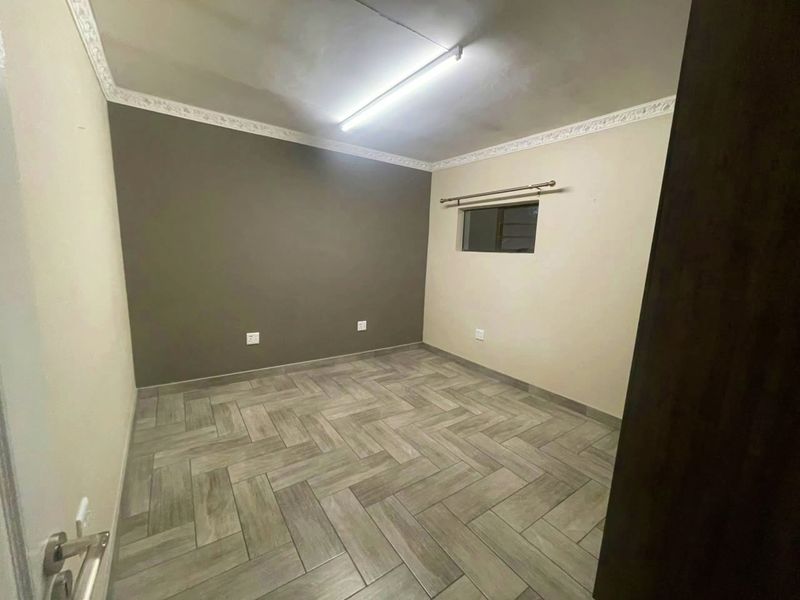 An empty bedroom featuring herringbone-patterned tile flooring, decorative ceiling cornices, and a neutral color palette, ready for personalization.