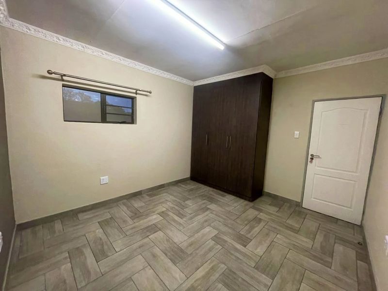A clean, empty bedroom featuring modern herringbone tile flooring, built-in dark wood cupboards, and decorative ceiling cornicing.