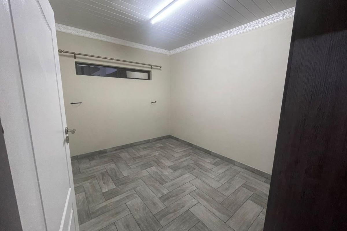 A clean, empty bedroom featuring modern herringbone-patterned tile flooring, a tongue and groove ceiling with decorative cornice, and a high-level horizontal window.