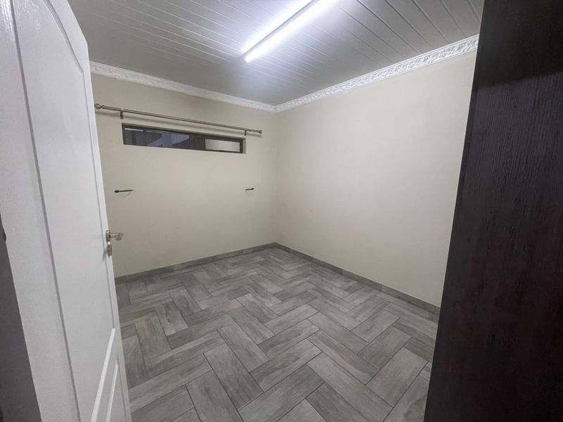 A clean, empty bedroom featuring modern herringbone-patterned tile flooring, a tongue and groove ceiling with decorative cornice, and a high-level horizontal window.