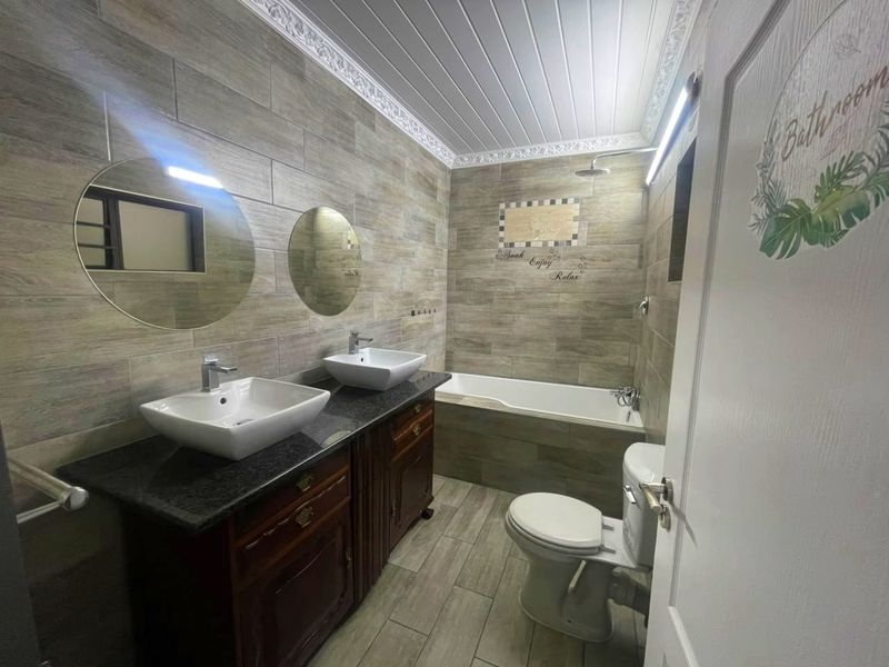 Modern bathroom featuring a double vanity with vessel sinks, granite countertop, built-in bathtub, shower, and stylish wood-look wall and floor tiling.