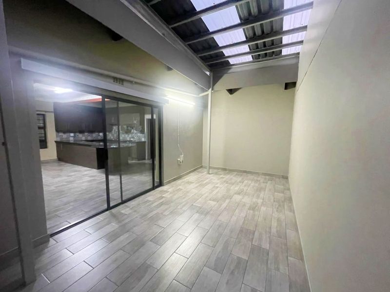 A covered patio area featuring modern tiled flooring, exposed structural beams, and translucent roof panels, providing seamless access to the interior living space.