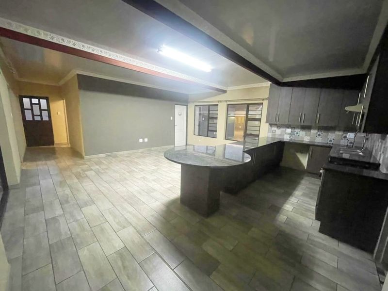 Spacious open-plan living and kitchen area featuring modern granite countertops, dark cabinetry, and neutral tiled flooring throughout.