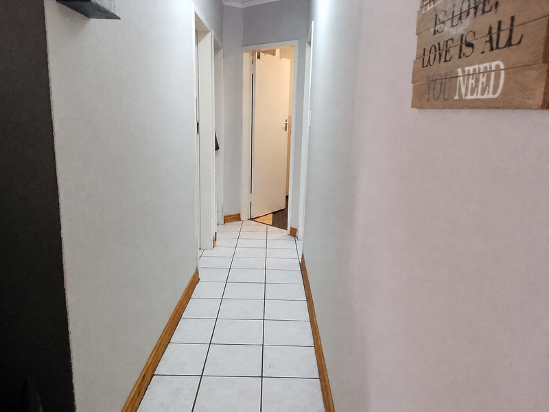 A clean and functional hallway featuring white tiled flooring and neutral wall finishes, providing access to multiple rooms within the apartment.