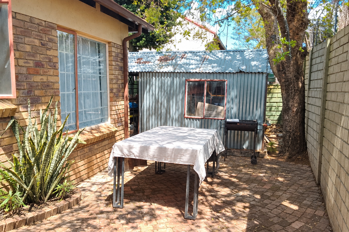 A rear courtyard area featuring brick paving, a face brick exterior wall, and a corrugated metal storage shed.