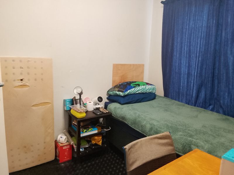 A compact bedroom featuring dark carpeting and blue curtains, requiring cosmetic updates to improve the overall presentation and appeal.