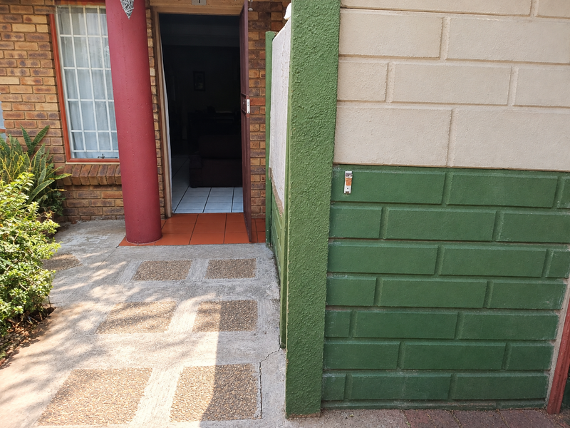 Front entrance area featuring brick facade, concrete paving, and a security gate, showing signs of wear on the exterior finishes.