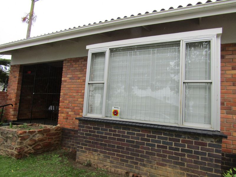 Front exterior view of the flat featuring a brick facade, security bars on windows, and a stone planter box.
