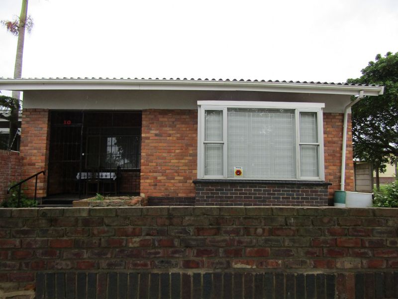 Front elevation of a brick-built flat featuring a covered entrance porch, security bars on windows, and a low brick boundary wall.
