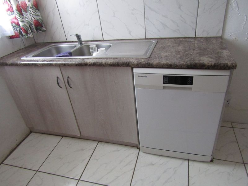 A functional kitchen area featuring a double bowl stainless steel sink, laminate countertops, built-in cabinetry, and tiled flooring and walls.