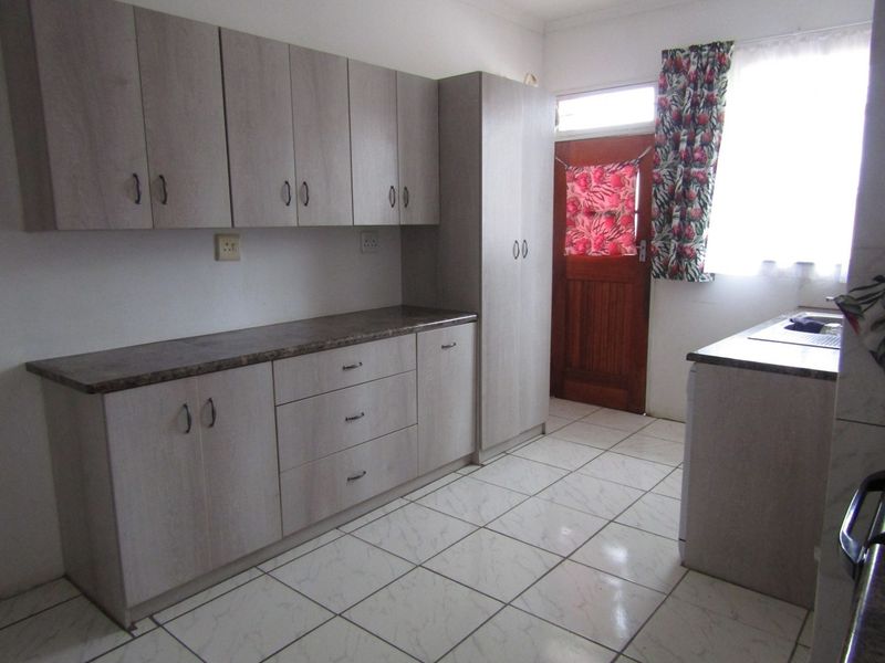 A functional kitchen featuring light-toned laminate cabinetry, durable laminate countertops, tiled flooring, and direct access to an exterior timber door.