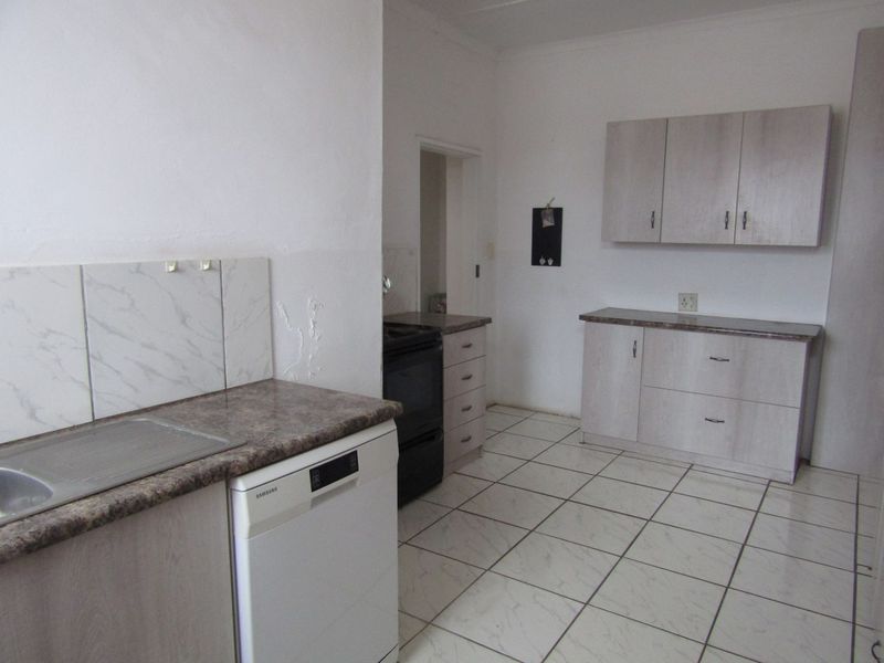 A functional kitchen featuring light-toned built-in cabinetry, laminate countertops, tiled flooring, and a tiled splashback, offering a clean and practical workspace.