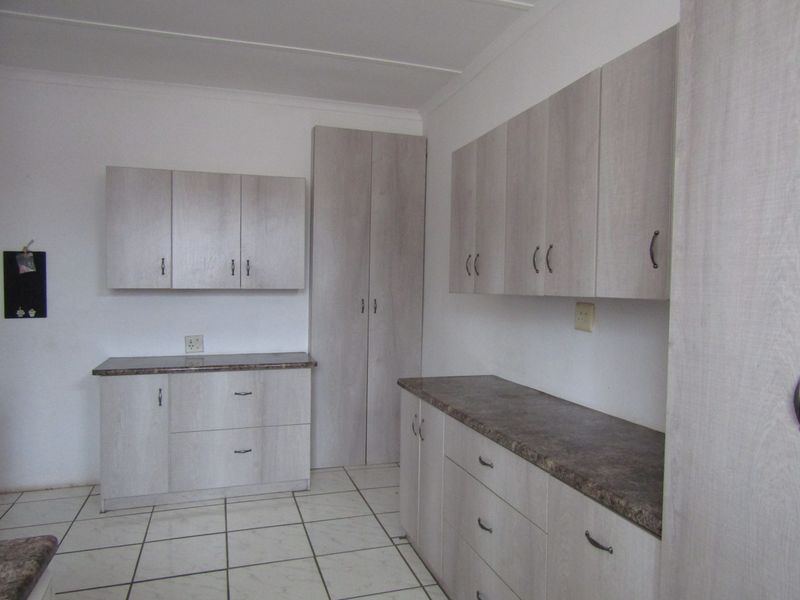A clean, functional kitchen area featuring light wood-look cabinetry, ample storage space, and durable tiled flooring.