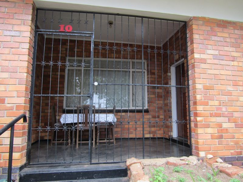 A covered patio area featuring exposed brick walls, concrete flooring, and a full-height security gate at the entrance.