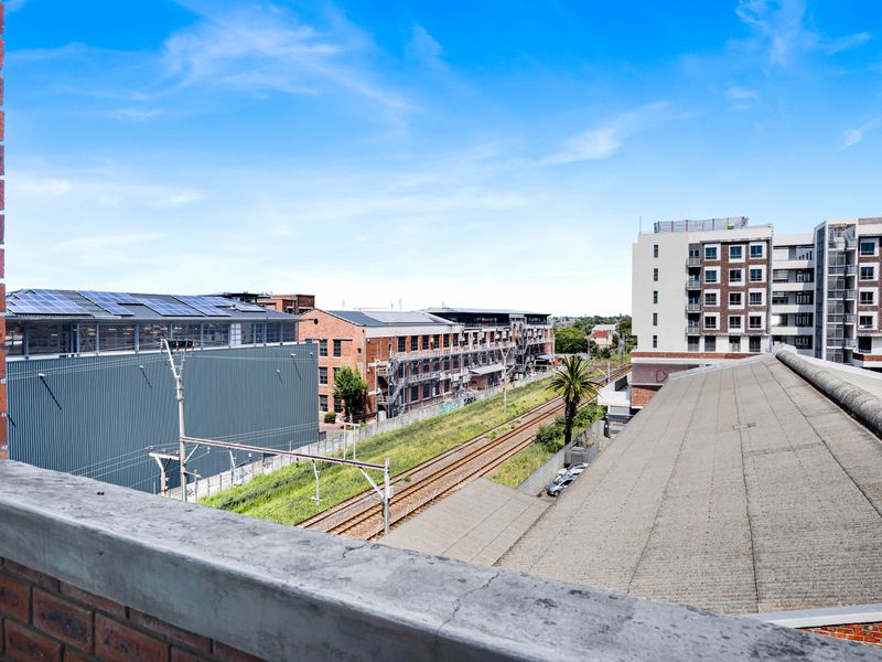 Elevated urban view overlooking railway tracks and surrounding industrial and residential buildings from a brick balcony.