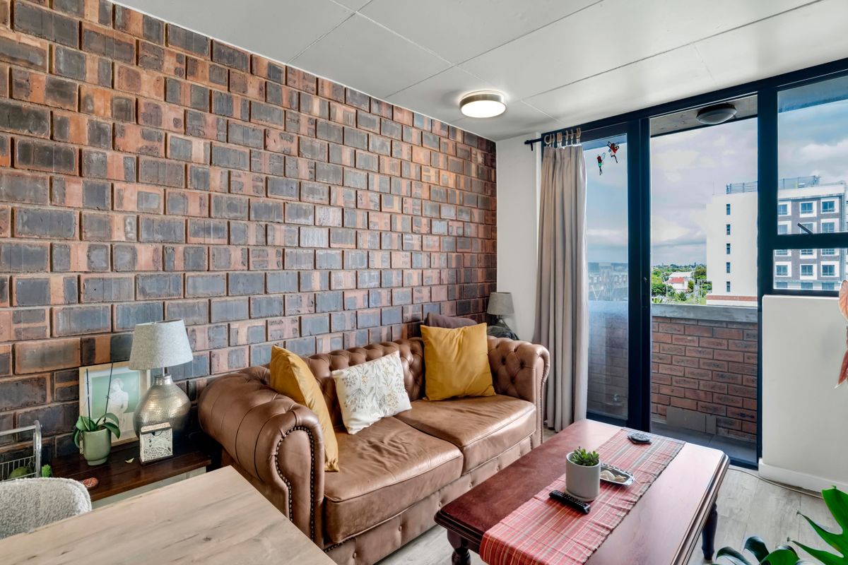 A cozy living room featuring a prominent exposed brick feature wall and large sliding glass doors providing access to an outdoor balcony area.