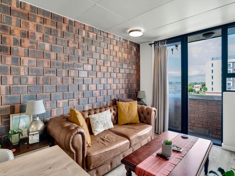 A cozy living room featuring a prominent exposed brick feature wall and large sliding glass doors providing access to an outdoor balcony area.