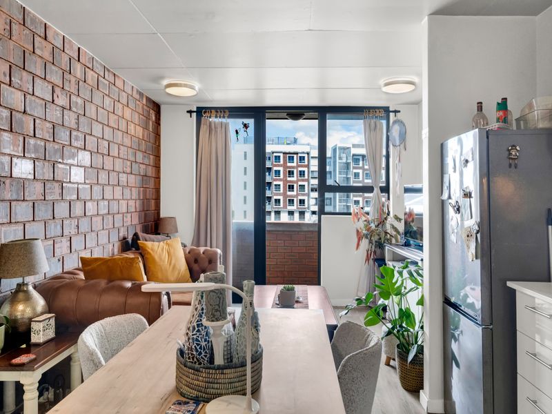 Open plan living and dining area featuring an exposed brick feature wall, laminate flooring, and direct access to a private balcony.