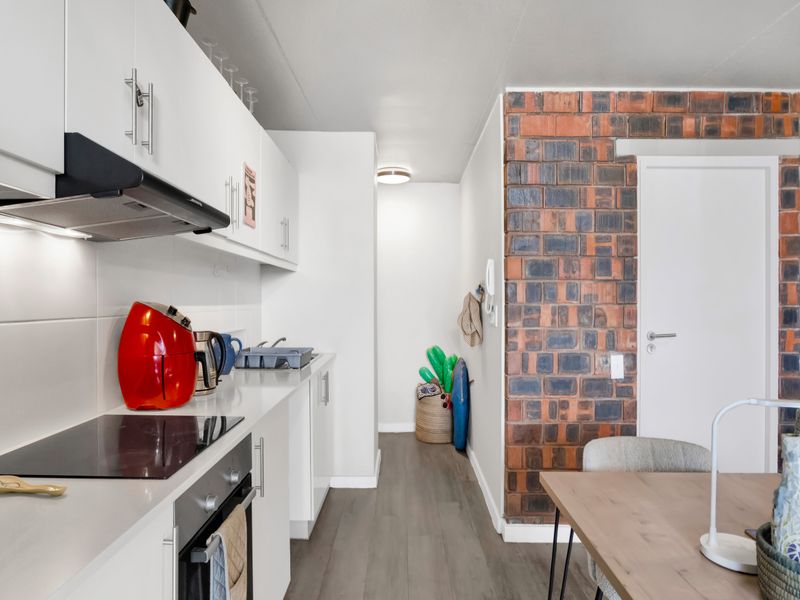 Open plan kitchen area featuring modern white cabinetry, integrated appliances, and a striking exposed brick feature wall, seamlessly connecting to the living space.