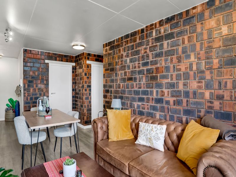 Open plan living and dining area featuring a prominent exposed brick feature wall and modern laminate flooring throughout.