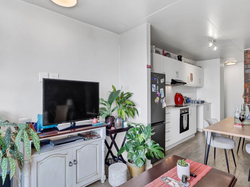 Open-plan living and kitchen area featuring modern white cabinetry, integrated appliances, laminate flooring, and a distinctive exposed brick feature wall.