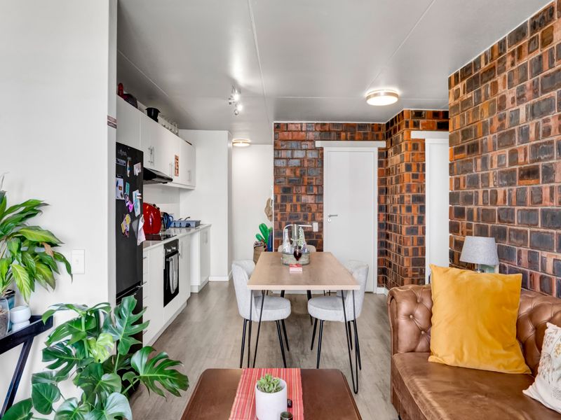 Open-plan living and dining area featuring a striking exposed brick wall, modern white kitchen cabinetry, and durable laminate flooring throughout the space.