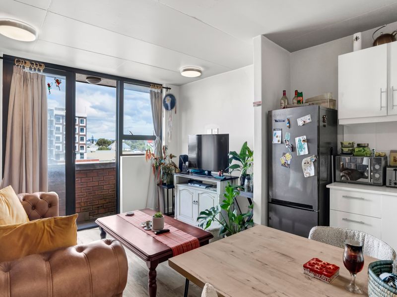 Open plan living and kitchen area featuring laminate flooring, modern cabinetry, and a sliding glass door leading to a balcony with urban views.