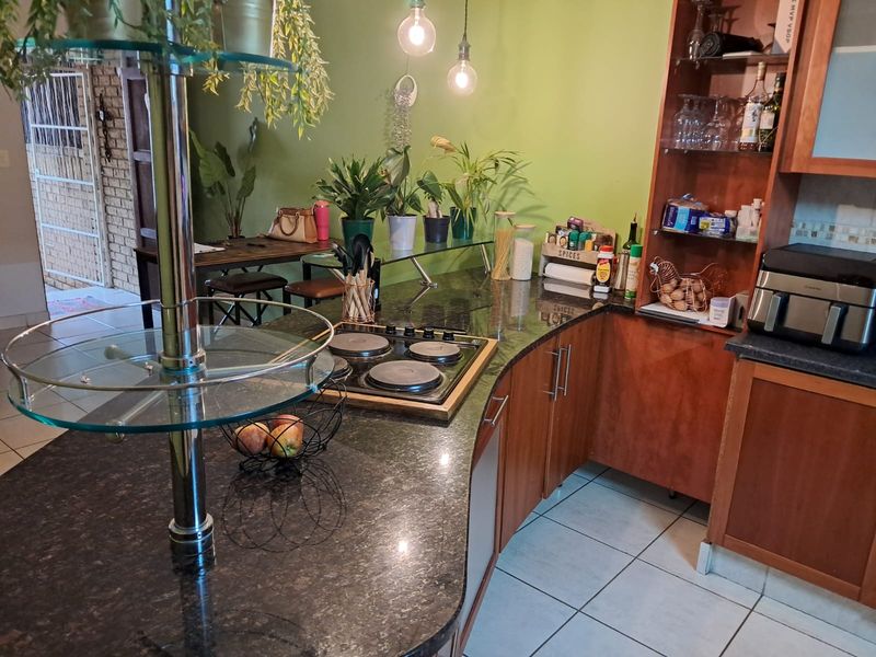 A functional kitchen featuring granite countertops, a built-in electric hob, and wooden cabinetry, complemented by tiled flooring and pendant lighting.