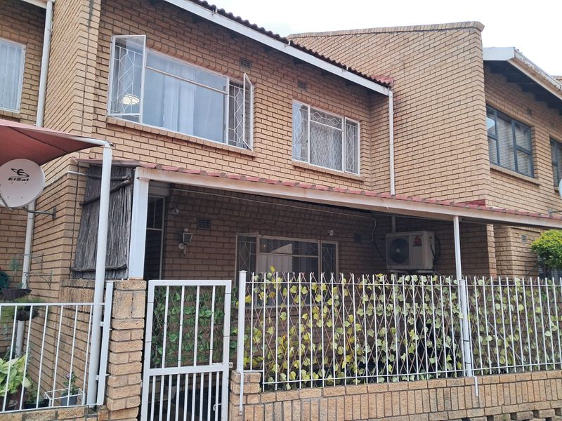 Front elevation of a face brick apartment unit featuring a covered patio area, security gates, and installed air conditioning unit.